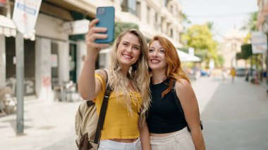 Two women hugging each other making selfie by smartphone at street