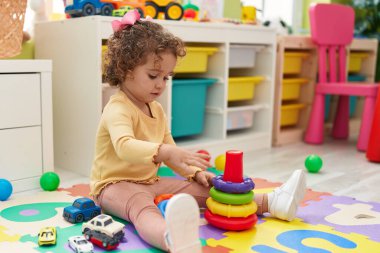 Adorable hispanic toddler playing with hoops toy sitting on floor at kindergarten