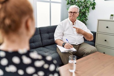 Senior psychologist man at consultation office cheerful with a smile on face pointing with hand and finger up to the side with happy and natural expression 