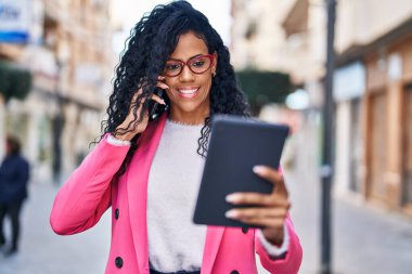Afrikalı Amerikalı kadın yönetici, elinde touchpad ile akıllı telefondan konuşuyor.