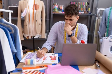 Young hispanic man tailor drawing clothing design at atelier