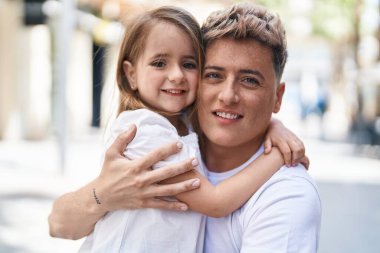 Baba ve kızı gülümsüyor. Parkta birbirlerine sarılıyorlar.