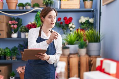 Çiçekçide panoya yazı yazan genç bir kadın.