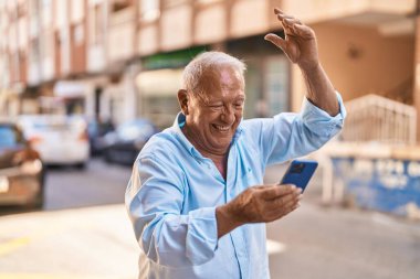 Senior grey-haired man using smartphone with cheerful expression at street