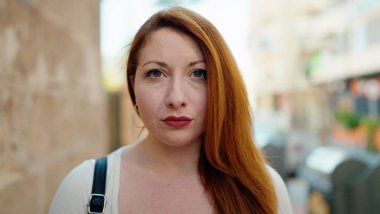 Sokakta duran rahat yüzlü, genç kızıl saçlı kadın.