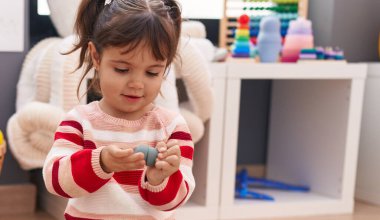 Adorable hispanic girl playing with toys sitting on floor at kindergarten