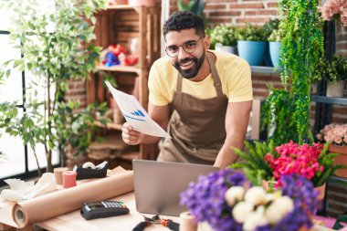 Young arab man florist using laptop reading document at florist