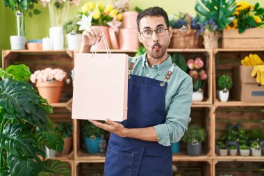 Handsome hispanic man working at florist shop making fish face with mouth and squinting eyes, crazy and comical. 