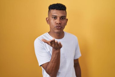 İspanyol asıllı genç adam sarı arka planda durup kameraya bakarak havada bir öpücük savuruyor ve sevimli ve seksi oluyor. aşk ifadesi. 