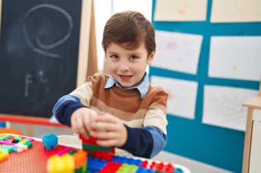 Anaokulundaki masada oturan, inşaat bloklarıyla oynayan sevimli İspanyol çocuk.