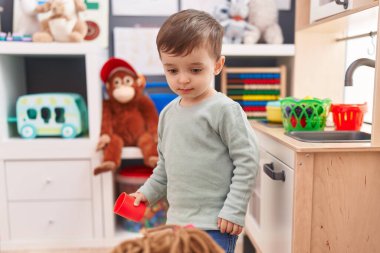 Adorable hispanic boy playing with play kitchen standing at kindergarten