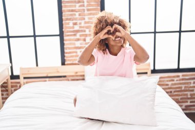 Afro-Amerikan kadın kalp hareketi yapıyor. Yatak odasında oturuyor.