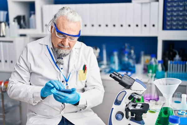 Middle age grey-haired man scientist smiling confident using smartphone at laboratory