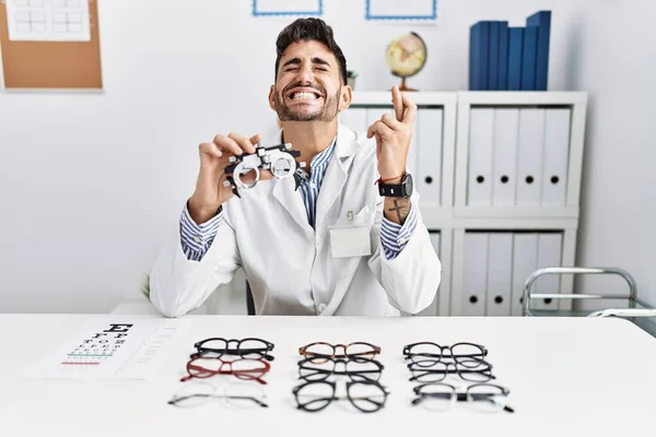Young Optician Man Holding Optometry Glasses Gesturing Finger Crossed Smiling — 图库照片