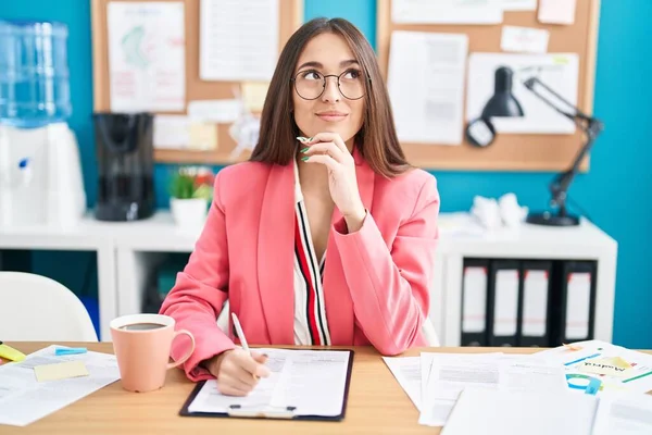 若いヒスパニック系の女性は オフィスで質問 集中的な表現について考える顎に手で眼鏡をかけて作業 思慮深い顔で笑顔 疑わしい概念 — ストック写真