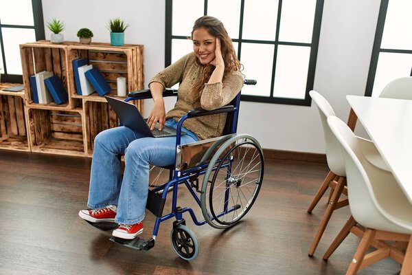 Young beautiful hispanic woman using laptop sitting on wheelchair at home