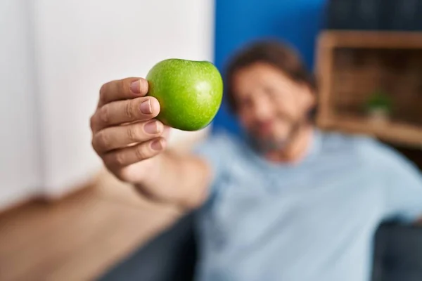 Middle age man holding apple sitting on sofa at home