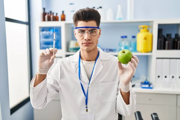 Young Hispanic Man Working Scientist Laboratory Holding Apple Skeptic Nervous — Stok fotoğraf