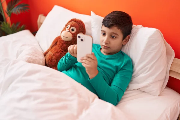 Adorável Menino Hispânico Usando Smartphone Deitado Cama Com Boneca Macaco — Fotografia de Stock