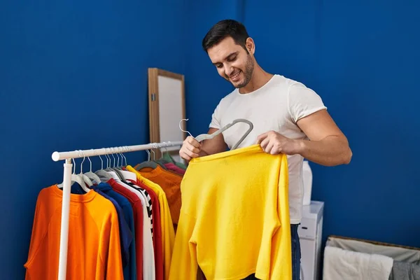 Young hispanic man putting clothes on clothes rack at laundry room