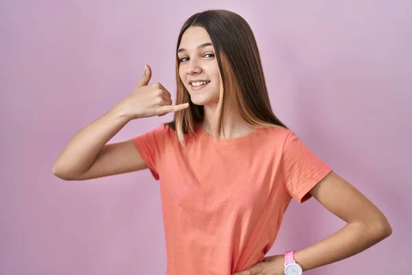 10代の女の子ピンクの背景に立って手や指で電話で話をするような携帯電話のジェスチャーを行う笑顔 コミュニケーションの概念 — ストック写真