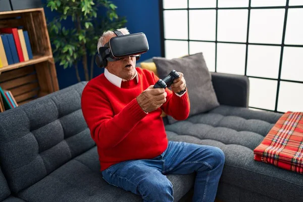 Senior man playing video game using virtual reality goggles at home