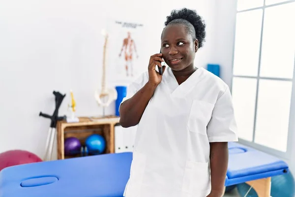 Young African American Woman Wearing Physiotherapist Uniform Talking Smartphone Clinic — Stockfoto
