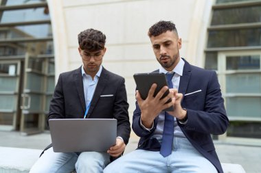Two hispanic men business workers using touchpad and laptop working at street