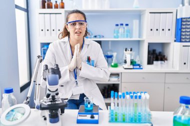 Young hispanic woman working at scientist laboratory begging and praying with hands together with hope expression on face very emotional and worried. begging. 