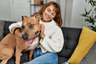 Beyaz bir kadın gülümsüyor. Kendine güvenen bir köpek. Evdeki kanepede oturuyor.