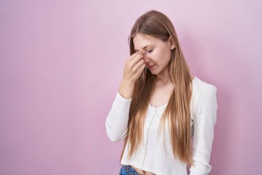 Pembe arka planda duran beyaz bir kadın yorgun burnu ve gözleri ovuşturup yorgunluk ve baş ağrısı çekiyor. Stres ve hüsran kavramı. 