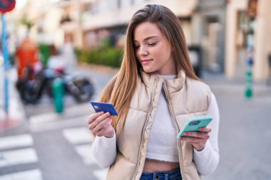 Sokakta akıllı telefon ve kredi kartı kullanan genç sarışın kadın.