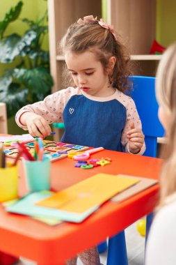 Adorable blonde girl playing with maths puzzle game sitting on table at kindergarten