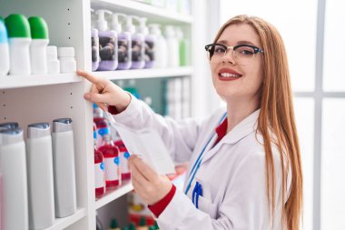 Young redhead woman pharmacist reading prescription at pharmacy