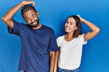 Young hispanic couple standing together confuse and wonder about question. uncertain with doubt, thinking with hand on head. pensive concept. 