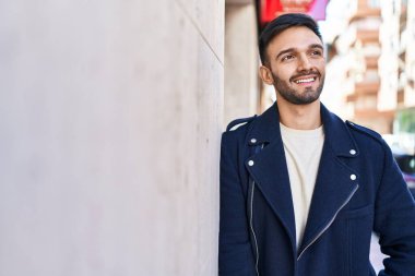 Young hispanic man smiling confident looking to the side at street