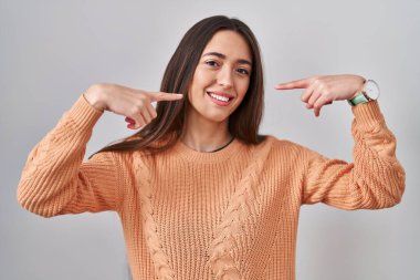 Young brunette woman standing over white background smiling cheerful showing and pointing with fingers teeth and mouth. dental health concept. 