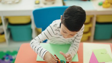 Anaokulunda masa başında oturmuş kağıda resim çizen sevimli İspanyol çocuk.