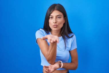 Brunette young woman standing over blue background looking at the camera blowing a kiss with hand on air being lovely and sexy. love expression. 