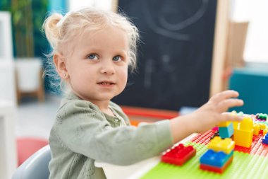 Adorable blonde girl playing with construction blocks sitting on table at kindergarten