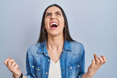 Mavi arka planda dikilen İspanyol kadın deli gibi bağırıyor ve bağırıyor. Saldırgan bir ifade ve kollar havada. hüsran kavramı. 