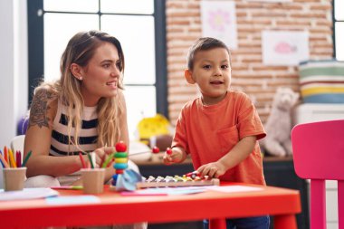 Öğretmen ve çocuk anaokulunda masada oturmuş ksilofon oynuyorlar.
