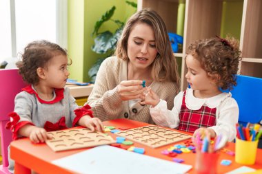 Teacher with girls playing with maths puzzle game sitting on table at kindergarten