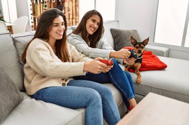 İki kadın evde köpekle oturup video oyunu oynuyor.