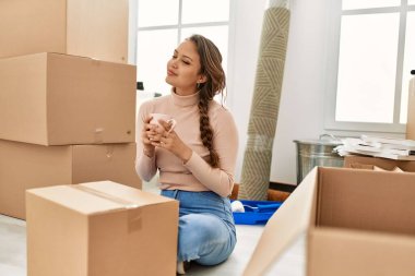 Genç, güzel, İspanyol bir kadın. Yeni evinde yerde oturmuş kahve içiyor.