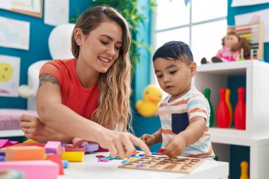 Teacher and toddler playing with maths puzzle game sitting on table at kindergarten