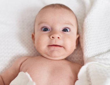 Adorable caucasian baby lying on bed with relaxed expression at bedroom