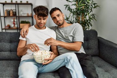 Evdeki kanepede oturup film izleyen iki İspanyol erkek.