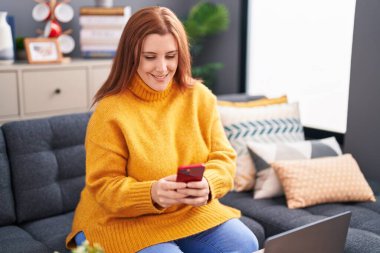 Young beautiful plus size woman using smartphone sitting on sofa at home
