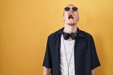 Sarı arka planda güneş gözlüğü takan genç beyaz bir adam kızgın ve öfkeli bağırıyor, öfkeyle bağırıyor. öfke ve agresif konsept. 